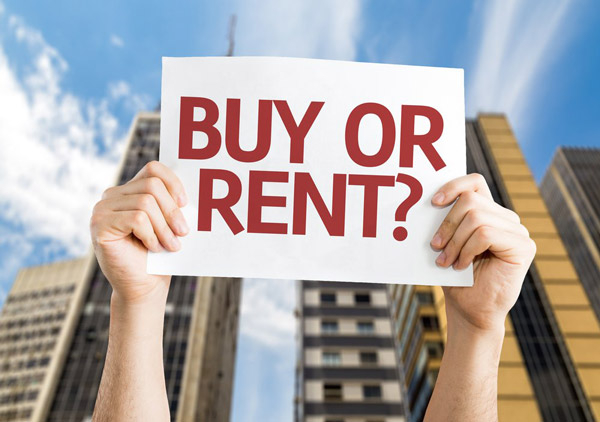 Person holding up a sign in front of commercial building that says, "Buy or Rent?"