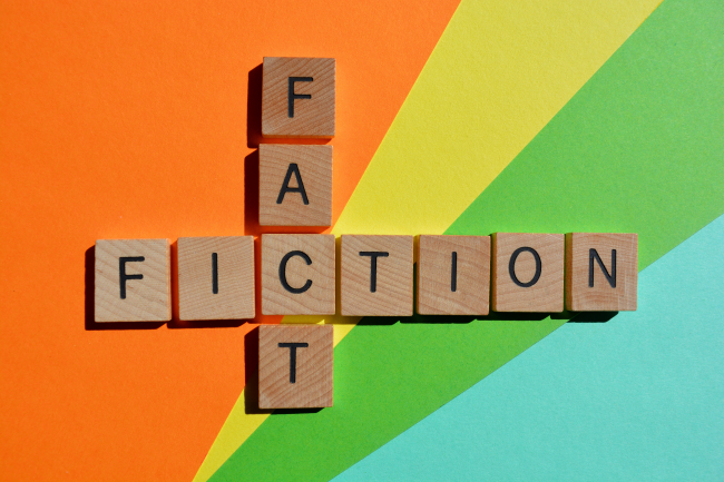 Scrabble tiles spelling "fact" vertically and "fiction" horizontally intersecting at the "C" on a rainbow colored background